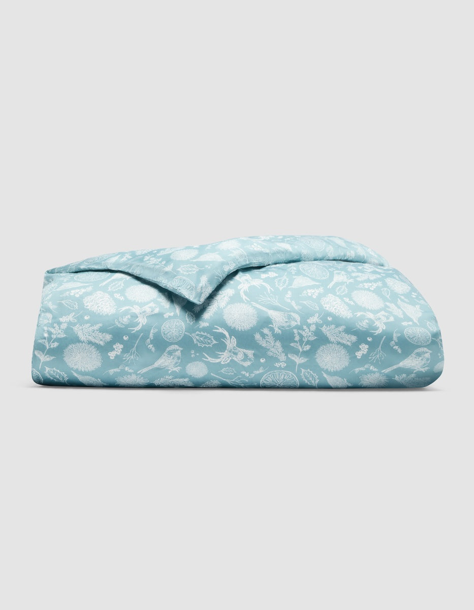 Folded light blue Cozy Earth Bamboo Duvet Cover featuring a white repeating pattern of winter birds, pine branches, and berries.