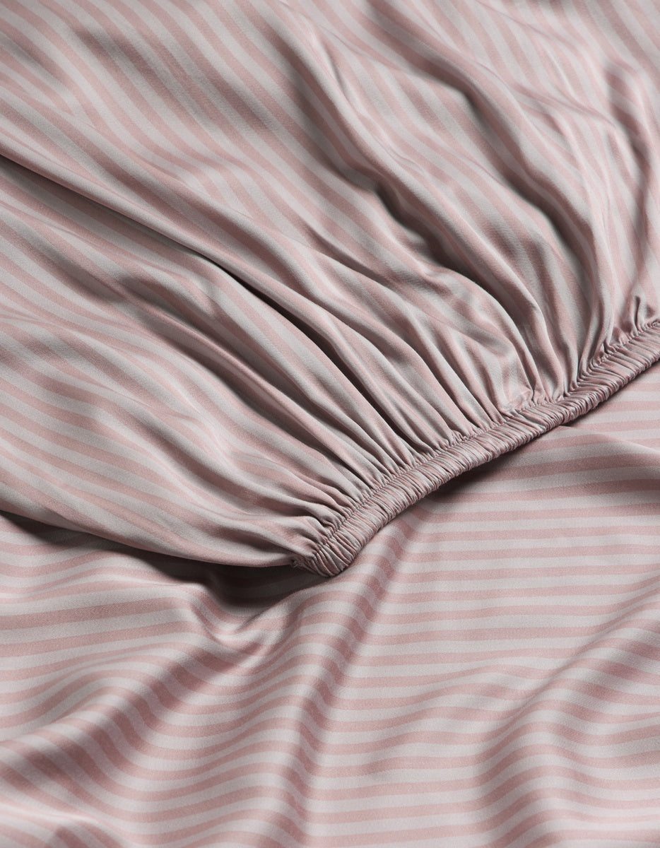 A close-up of the Cozy Earth Bamboo Fitted Sheet displays its lavender and grey diagonal stripes, featuring a gathered elastic edge and smooth, slightly wrinkled fabric.