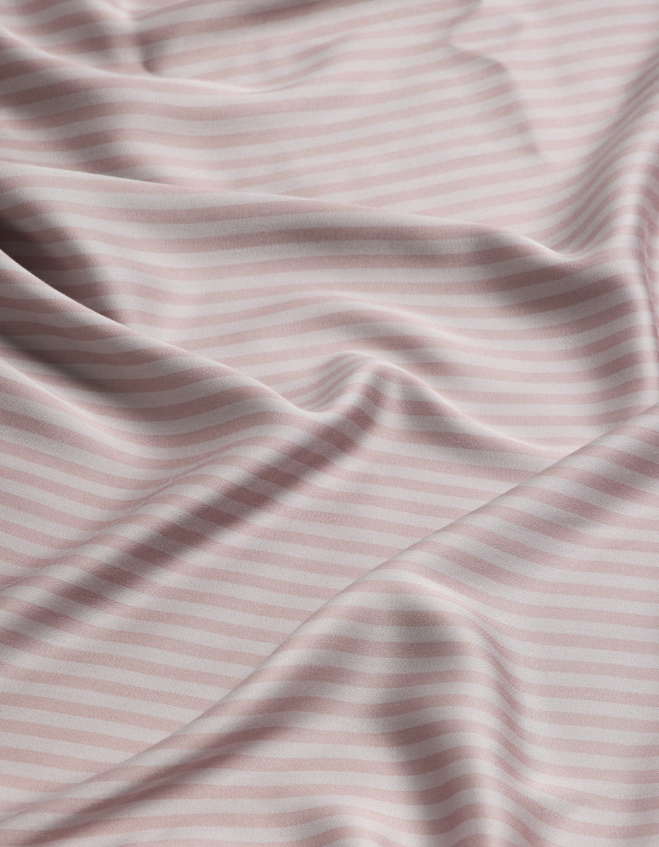 A close-up of a Cozy Earth Bamboo Flat Sheet in soft fabric with a pale pink and white horizontal stripe pattern, shown with loose folds and drapes.