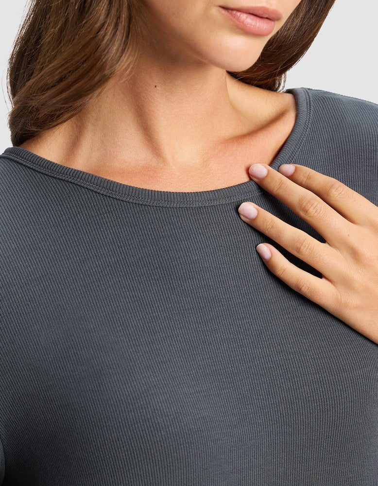 A woman in the Cozy Earth Women’s Bamboo Rib-Knit Boyfriend Sleep Dress in dark gray gently rests her manicured hand on her chest, with only her mouth, neck, and upper torso visible.