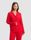 A woman with long brown hair stands against a light gray background, wearing the Cozy Earth Women's Bamboo Rib-Knit Classic Long Sleeve Pajama Top in red and matching pants. She smiles gently with one hand on her abdomen.|Color:Crimson