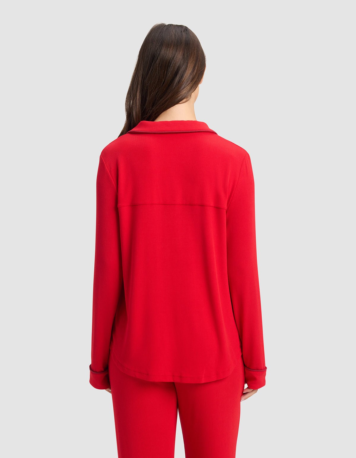 A woman with long brown hair, seen from behind, wears the Cozy Earth Women's Bamboo Rib-Knit Classic Long Sleeve Pajama Top in red, paired with matching pants against a plain light gray background.|Color:Crimson