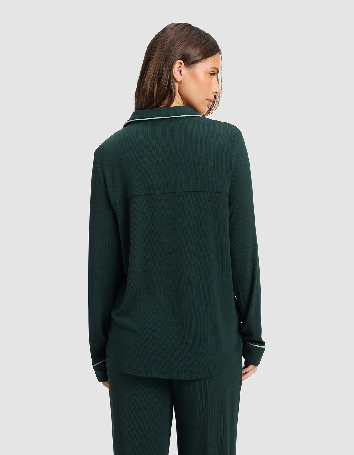 A woman with straight brown hair is seen from behind, wearing a Cozy Earth Women's Bamboo Rib-Knit Classic Long Sleeve Pajama Top in dark green with matching pants against a plain light gray background.|Color:Spruce