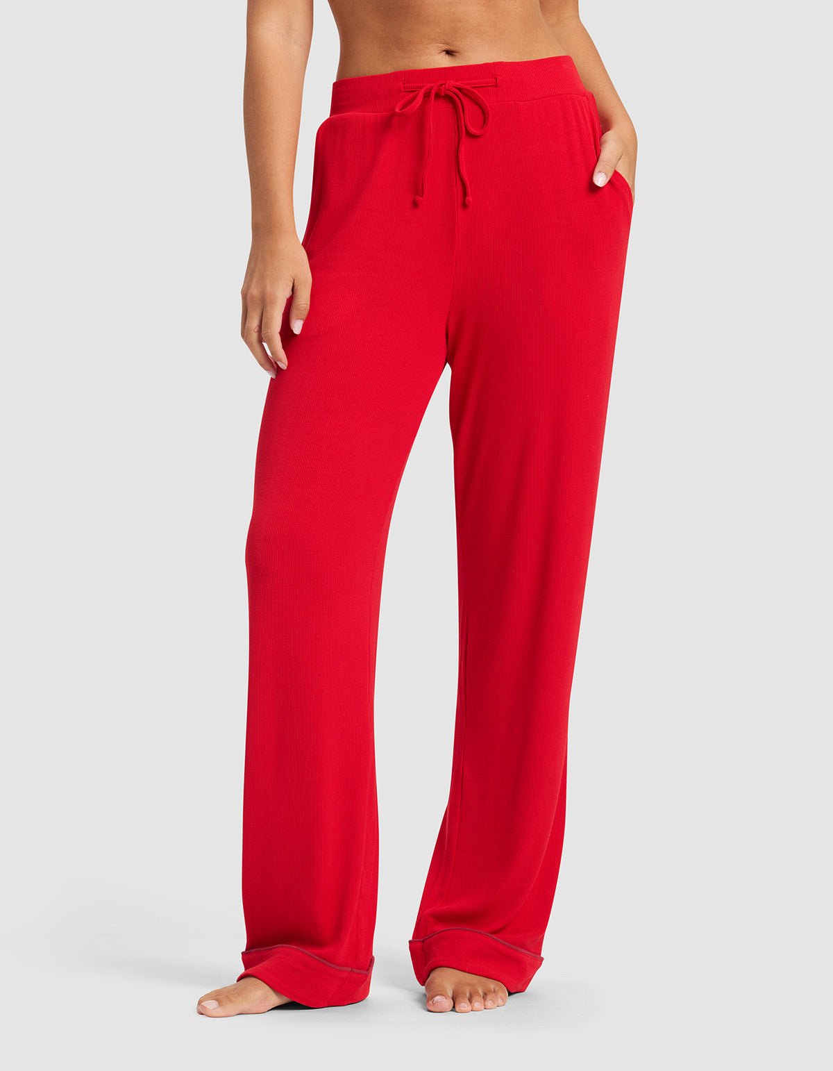 A person stands barefoot wearing Cozy Earth's Women's Bamboo Rib-Knit Classic Pajama Pant in bright red, featuring an adjustable drawstring waist and side pockets; their upper body is not visible.
