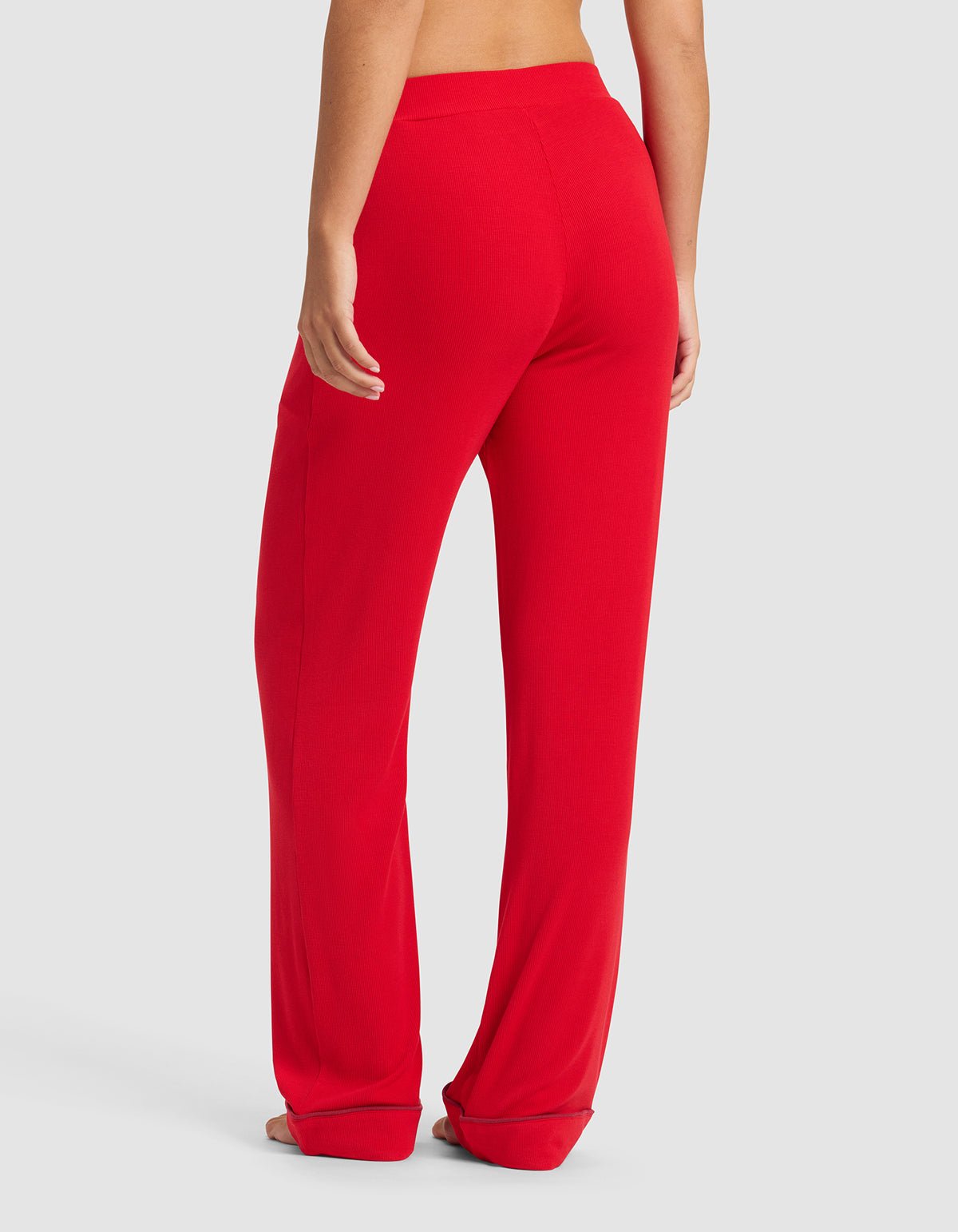 A person is shown from the waist down, wearing Cozy Earth's Women's Bamboo Rib-Knit Classic Pajama Pant in bright red with a relaxed fit and slight fabric pooling at the ankles, set against a plain white background.
