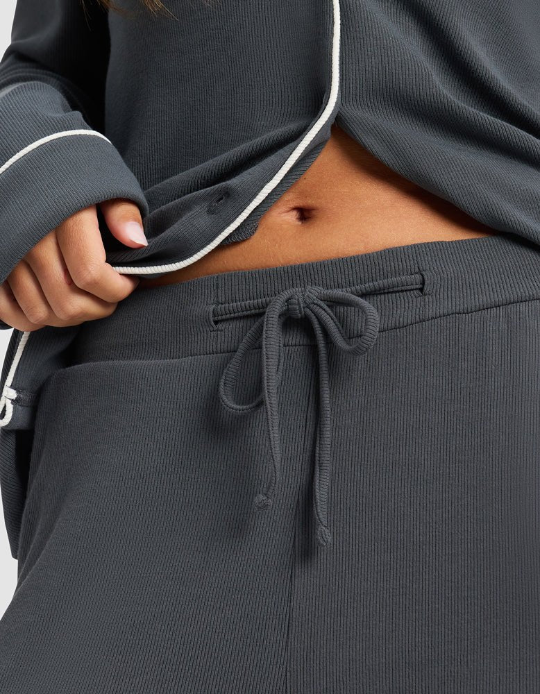 Close-up of a person wearing Cozy Earth's Women's Bamboo Rib-Knit Classic Pajama Pant in dark gray with a drawstring waist and matching long-sleeve top, slightly lifting the top to reveal part of their midriff.