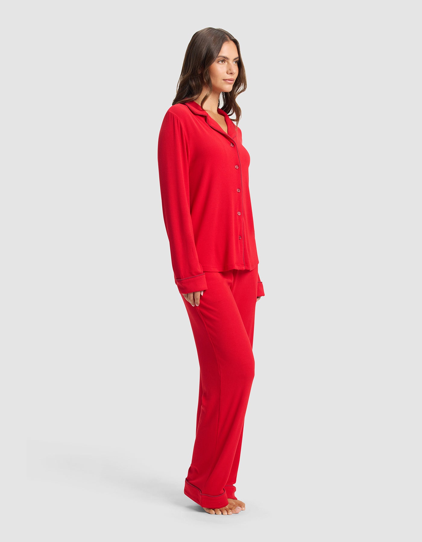 A woman stands barefoot against a plain light gray background, wearing the Cozy Earth Women's Bamboo Rib-Knit Classic Long Sleeve Pajama Set in red.|Color:Crimson