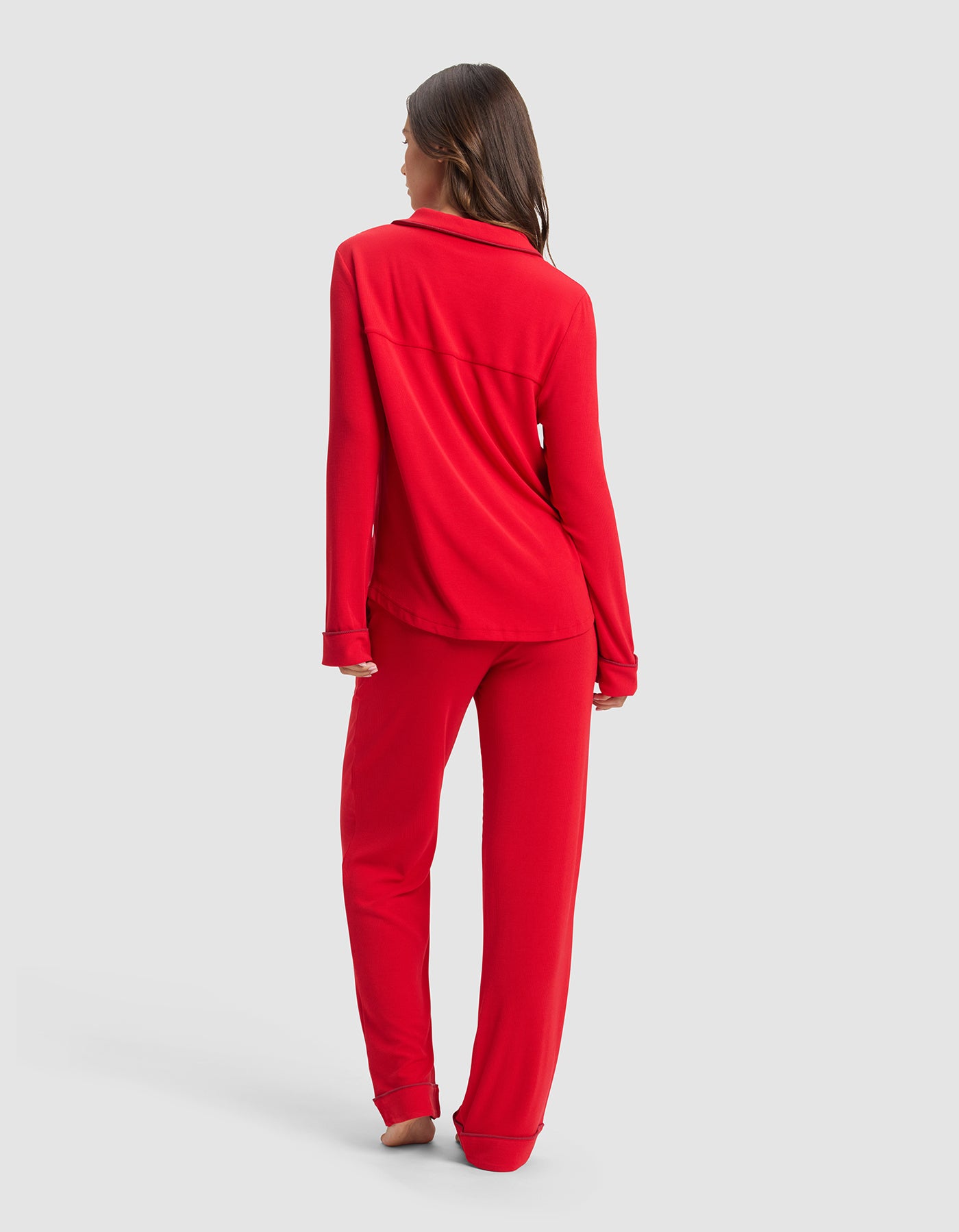 A woman stands barefoot, facing away, wearing the Cozy Earth Women's Bamboo Rib-Knit Classic Long Sleeve Pajama Set in red, set against a plain light gray background.|Color:Crimson