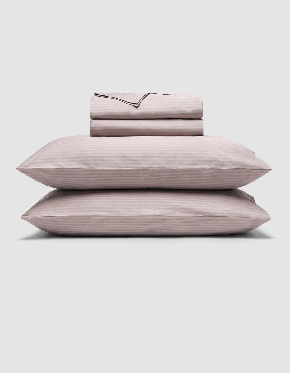 A Cozy Earth Bamboo Sheet Set in lavender stripe pattern, with two pillows in matching pillowcases stacked beneath neatly folded sheets, displayed on a plain white background.