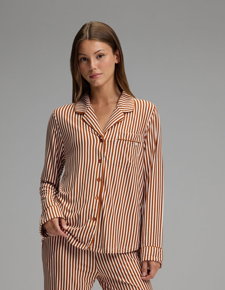A person stands facing the camera against a plain gray background, wearing the Cozy Earth Women’s Bamboo Stretch-Knit Long Sleeve Pajama Top, featuring matching brown and white vertical stripes.
