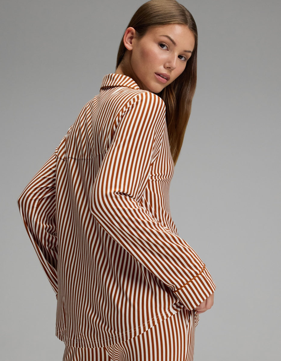 A woman with long brown hair poses sideways, looking over her shoulder against a plain gray background while wearing the Cozy Earth Women’s Bamboo Stretch-Knit Long Sleeve Pajama Top.