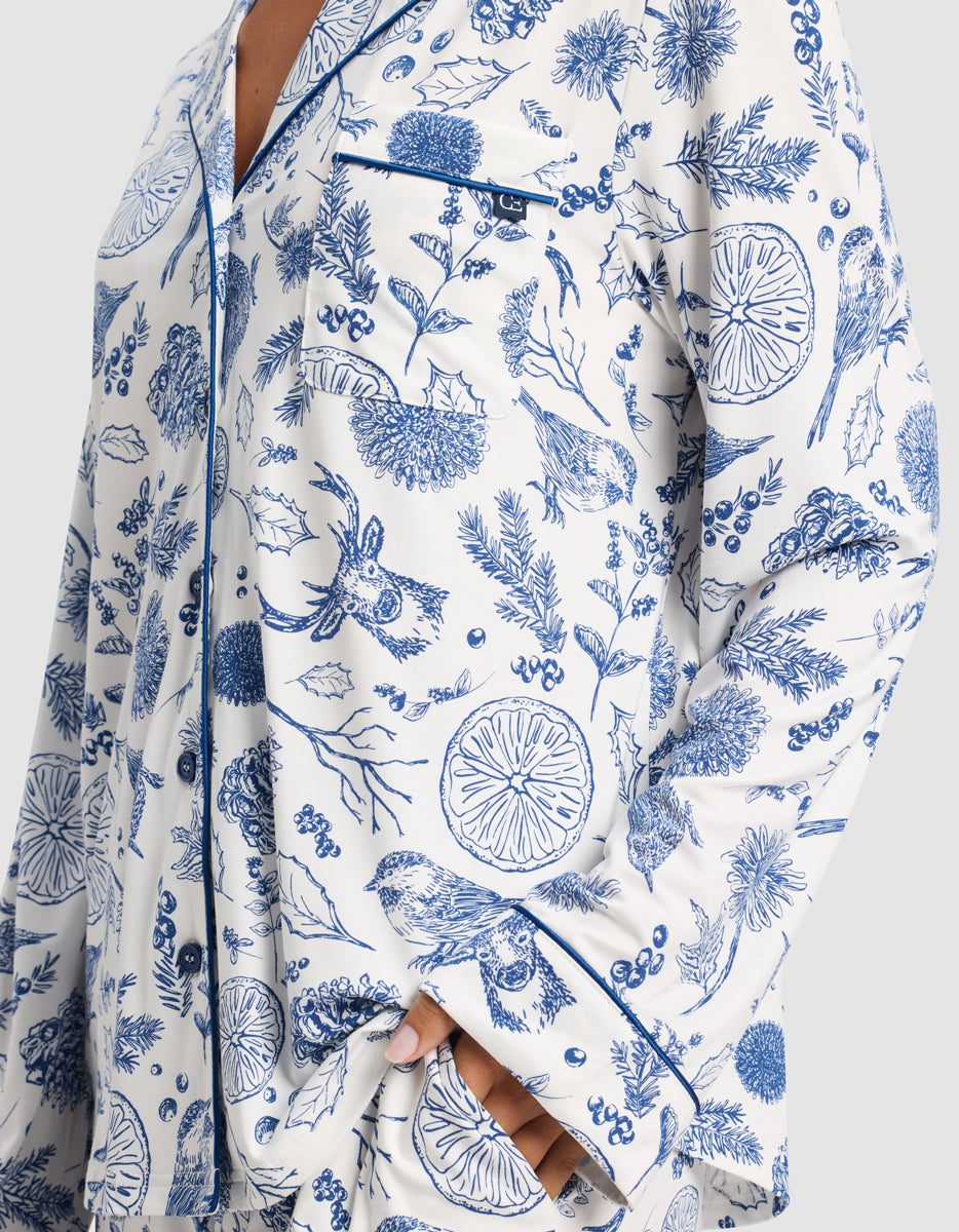 A close-up of a person wearing the Cozy Earth Women's Bamboo Stretch-Knit Long Sleeve Pajama Top in white with blue botanical and animal prints, chest pocket, and navy piping.