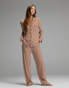 A person stands barefoot on a gray floor, wearing the Cozy Earth Women’s Bamboo Stretch-Knit Long Sleeve Pajama Set in brown-and-white vertical stripes, featuring loose-fitting long sleeves and pants, against a plain gray background.|Color:Market Stripe in Cinnamon