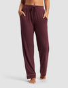 A woman wears Cozy Earth's Women's Bamboo Stretch-Knit Pajama Pant in burgundy, featuring a drawstring waist and pockets, standing barefoot against a plain gray background.|Color:Burgundy