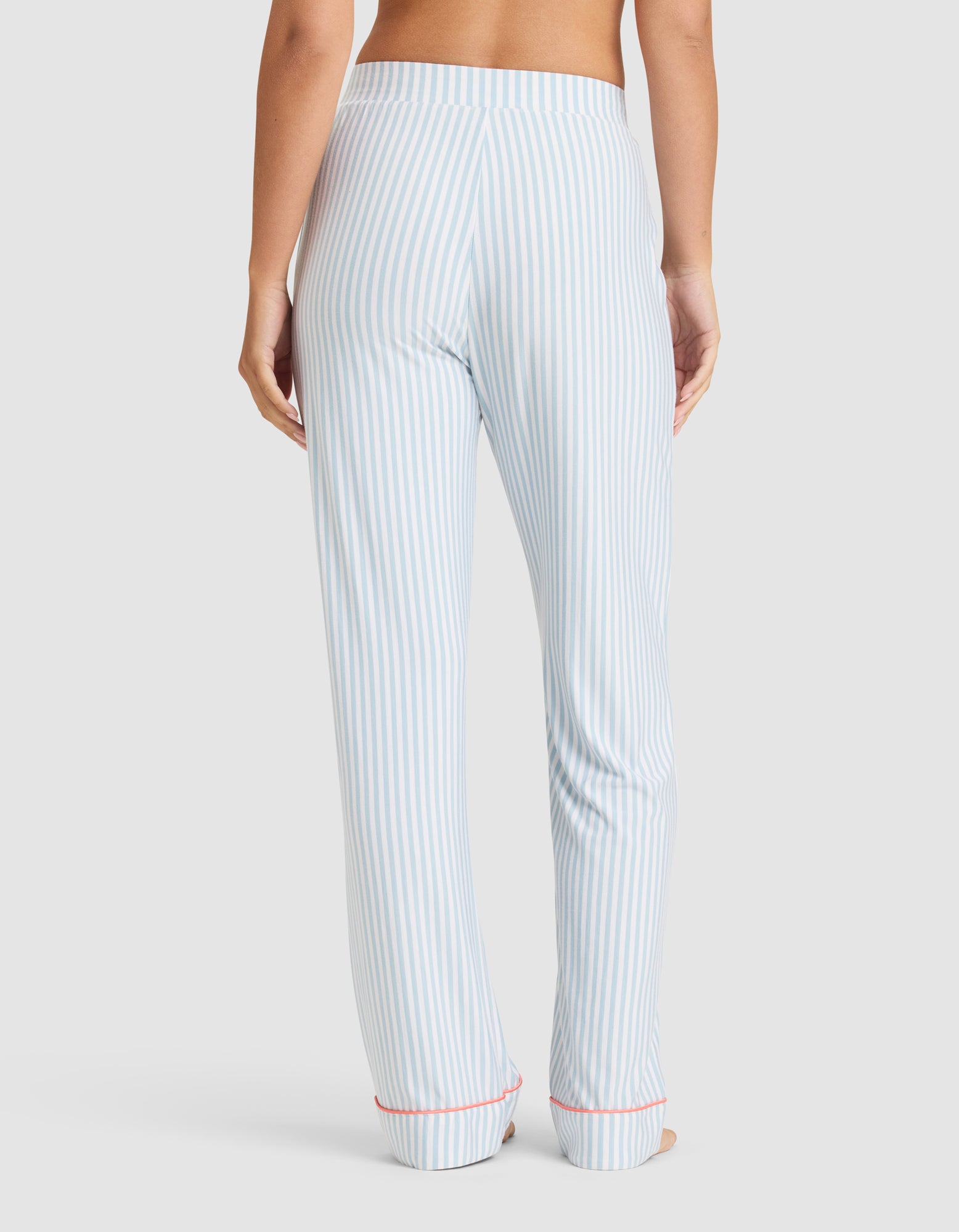 Model faces away, wearing Cozy Earth Women's Bamboo Stretch-Knit Long Sleeve Pajama Set in light blue and white vertical stripes with red cuff trim, set against a plain white background. 
