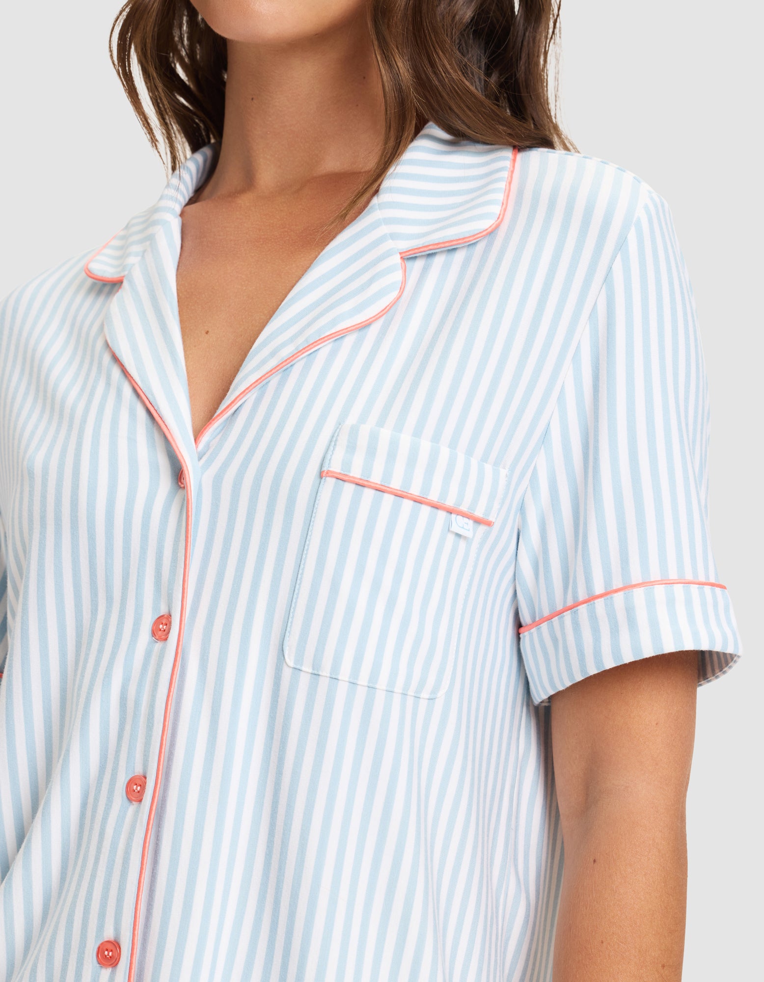 A woman wears a Cozy Earth Women's Bamboo Stretch-Knit Short Sleeve Pajama Set in light blue and white stripes with red piping. The image is cropped at the shoulders and mid-torso.