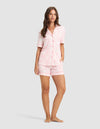 A woman stands barefoot in a HIDE Women's Bamboo Stretch-Knit Short Sleeve Pajama Top and matching light pink patterned shorts with pockets, set against a plain light gray background. |Color:Tulip Toile