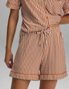 A person is shown from shoulder to mid-thigh wearing the Cozy Earth Women’s Bamboo Stretch-Knit Pajama Short, part of a matching short-sleeve button-up shirt and shorts set featuring vertical white and brown stripes.|Color:Market Stripe in Cinnamon