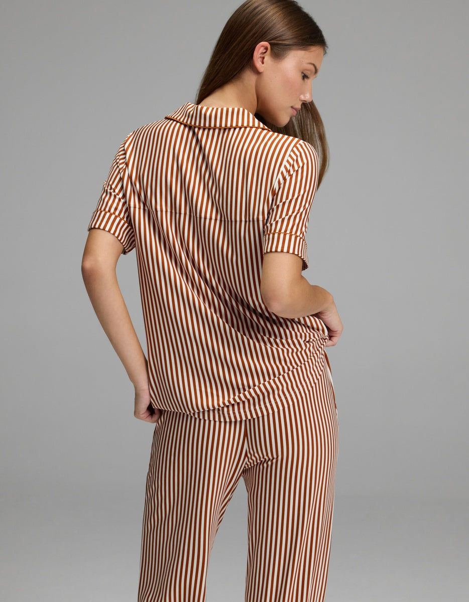 A person stands with their back to the camera, wearing the Cozy Earth Women’s Bamboo Stretch-Knit Short Sleeve Pajama Top paired with matching pants featuring vertical brown and white stripes. The background is plain gray.