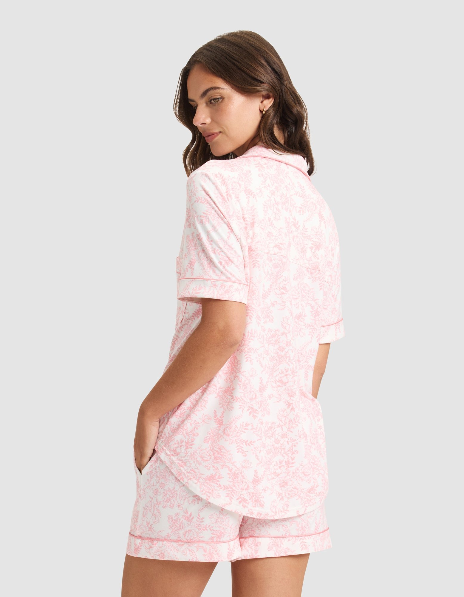A woman stands with her hands in the pockets of her HIDE Women's Bamboo Stretch-Knit Short Sleeve Pajama Top and matching shorts, looking over her shoulder against a plain background. 
