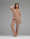 A woman stands barefoot against a plain gray background, wearing the Cozy Earth Women’s Bamboo Stretch-Knit Short Sleeve & Pant Pajama Set in matching brown and white vertical stripes.|Color:Market Stripe in Cinnamon