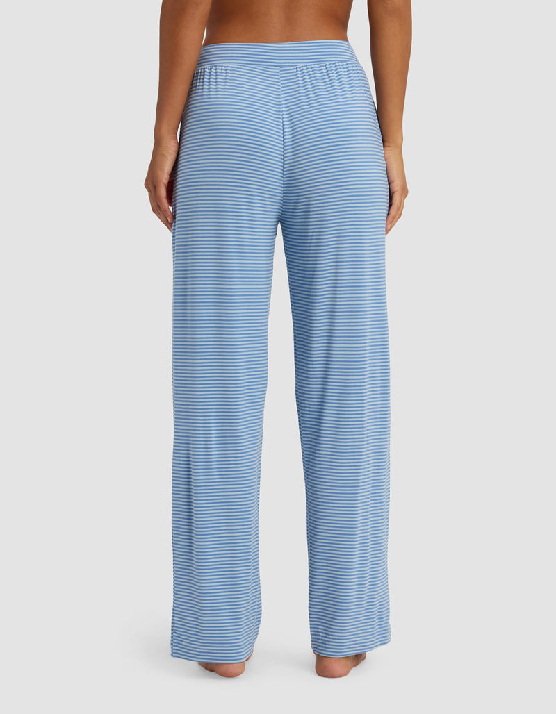 A woman is seen from the back, barefoot, wearing Cozy Earth's Women's Bamboo Stretch-Knit Pant in light blue and white stripes, standing against a plain white background.