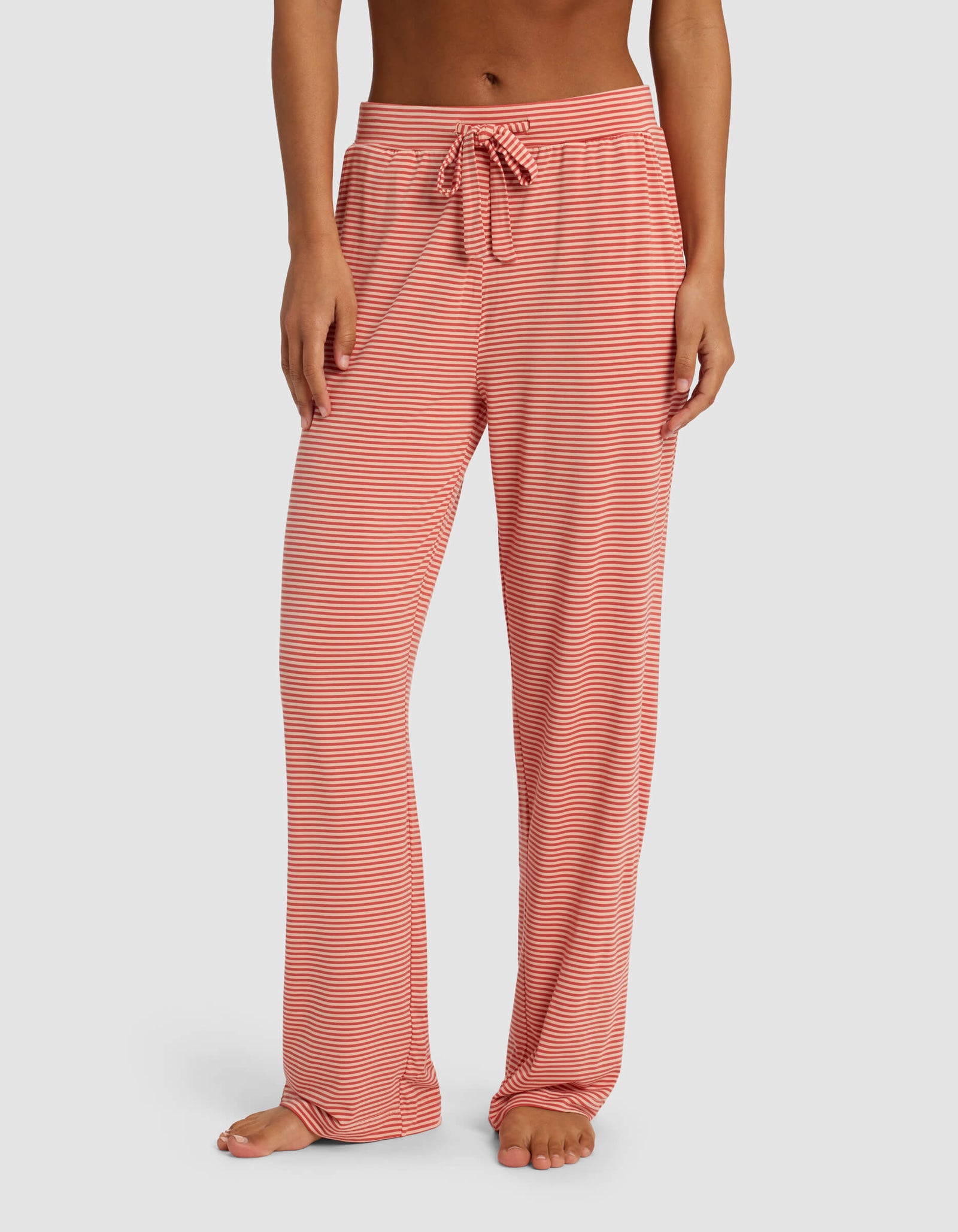 A woman is wearing Cozy Earth's Women's Bamboo Stretch-Knit Pant, featuring a loose fit and drawstring waist, standing barefoot against a plain background.