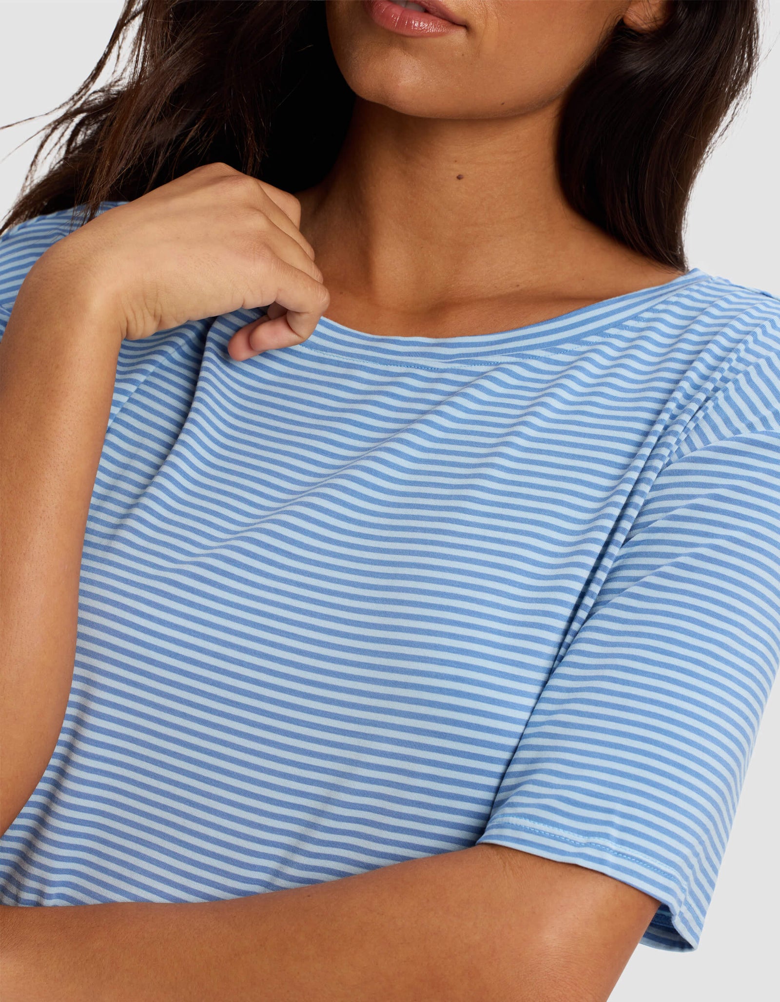 A woman wears the Cozy Earth Women's Bamboo Stretch Knit Sleep Dress in light blue and white stripes, touching her collar. Only her torso and part of her face are visible.