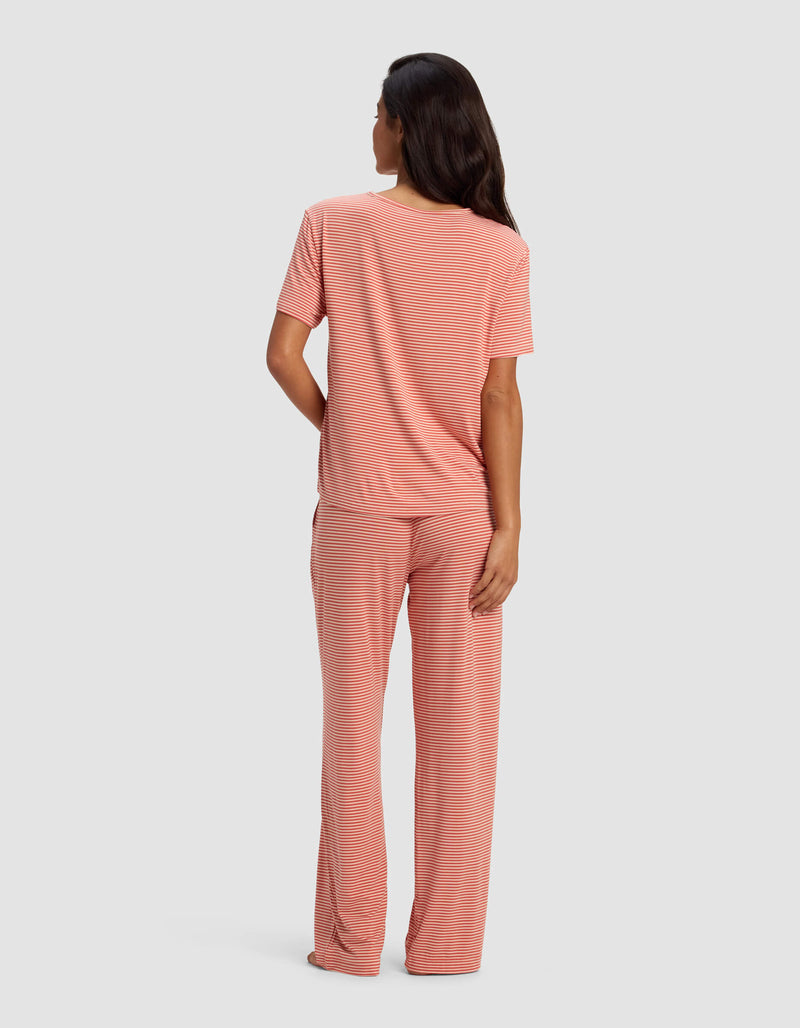 A woman faces away, wearing the Cozy Earth Women's Bamboo Stretch-Knit Lounge Tee & Pant Set in light pink and white stripes. The background is a plain light gray.