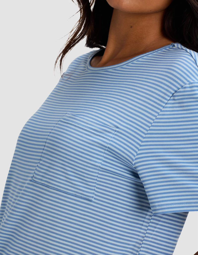 A woman wears the Cozy Earth Women's Bamboo Stretch-Knit Lounge Tee in light blue and white stripes with a chest pocket. The image is cropped to highlight the shirt's design and texture on her upper body.