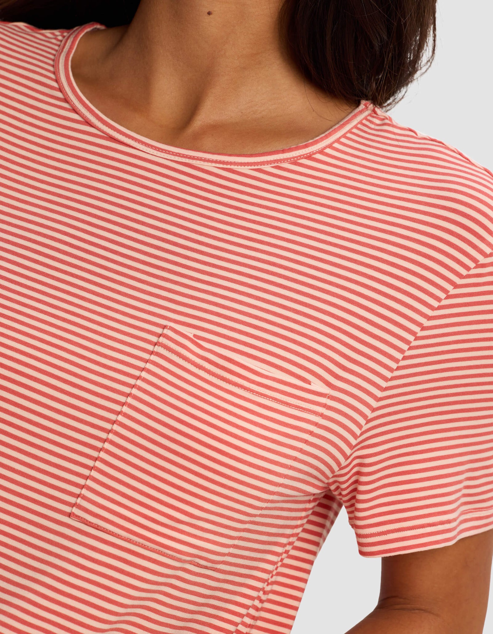 Close-up of a woman wearing the Cozy Earth Women's Bamboo Stretch-Knit Lounge Tee in pink and white stripes, featuring a round neckline and small chest pocket; only her neck, shoulder, and upper torso are visible.
