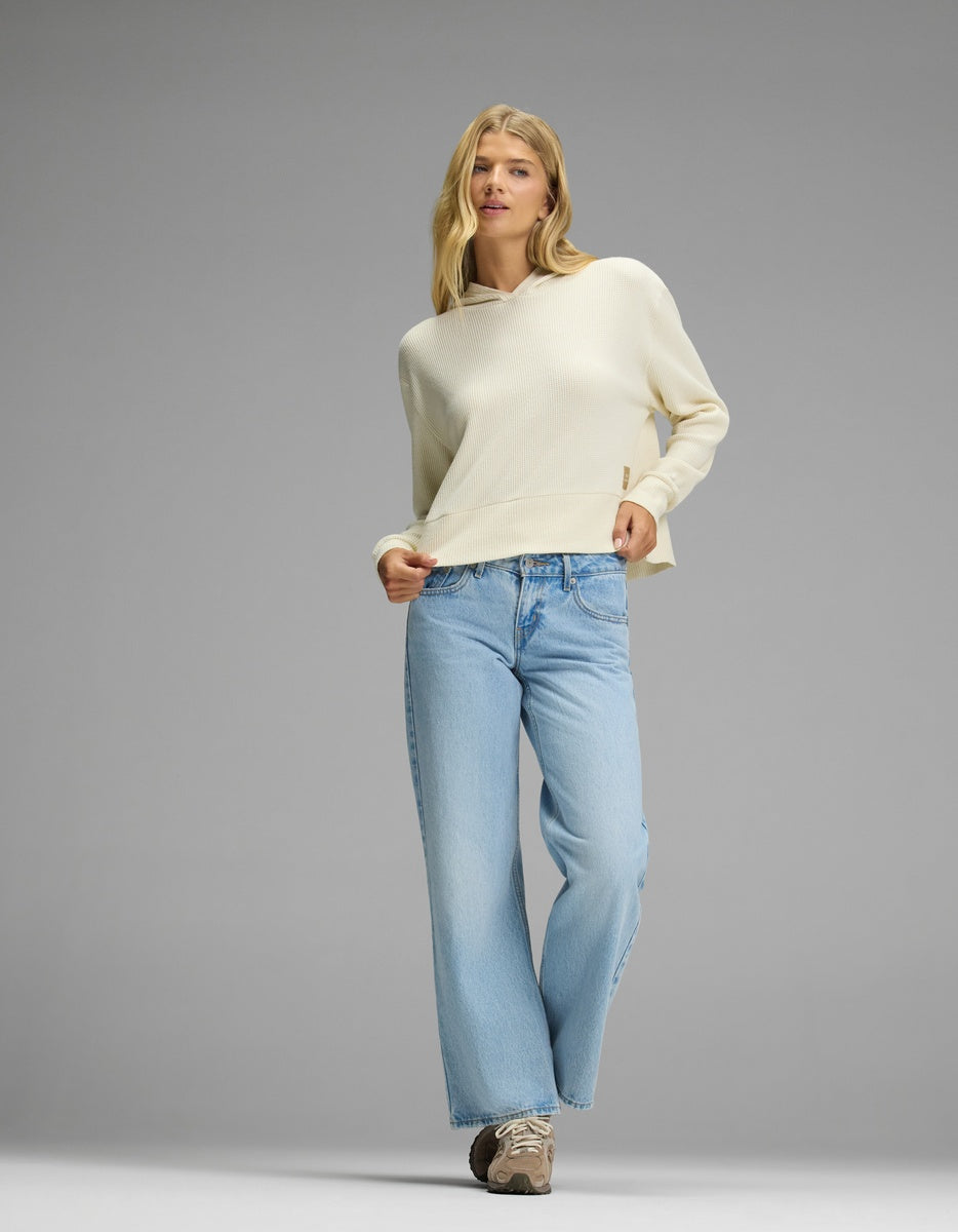 A person wearing a cream-colored Cozy Earth Women’s Blake Waffle Hoodie and light-wash blue jeans.