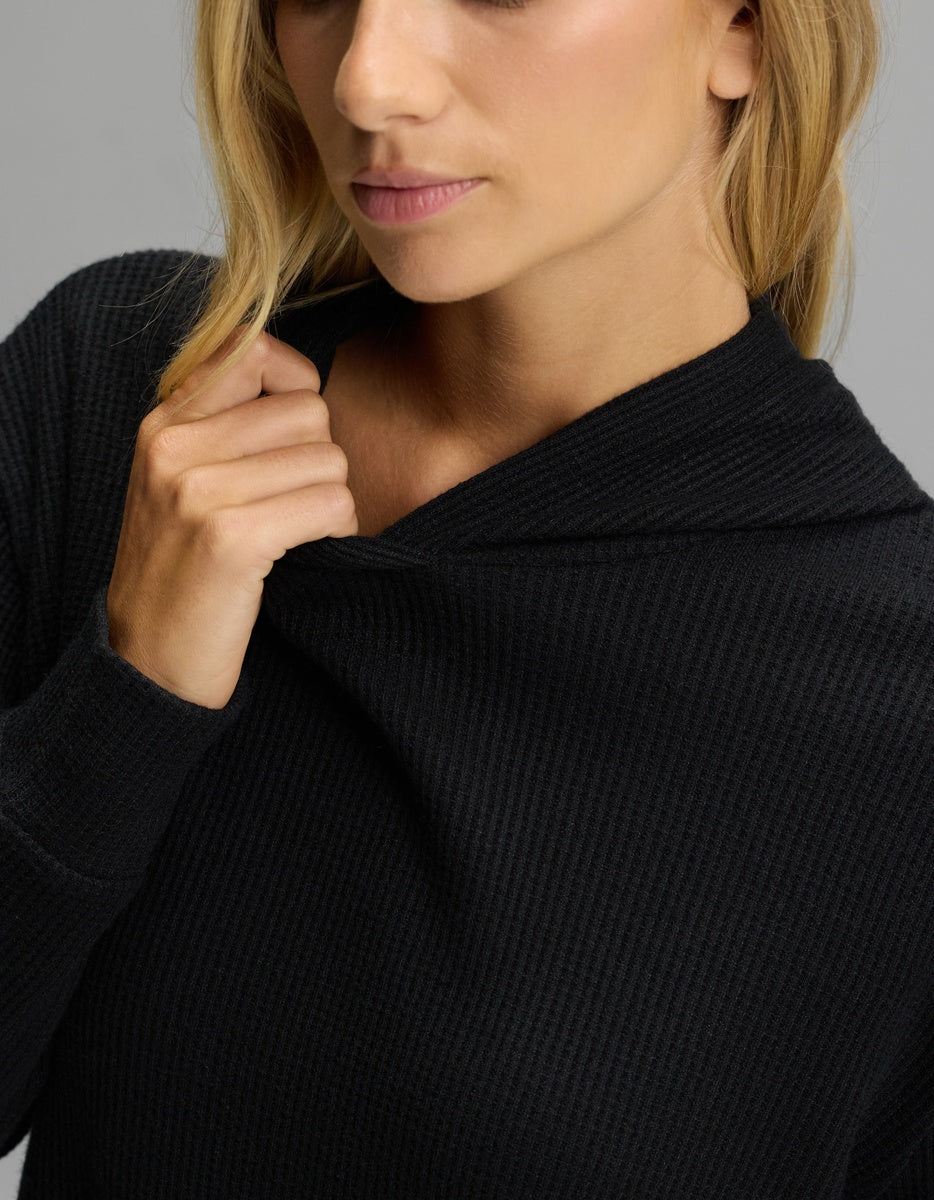 A person wearing a black Women’s Blake Waffle Hoodie, pulling the collar toward their neck.