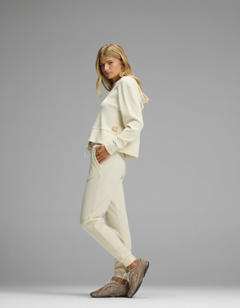 A woman models the cream-colored Women’s Blake Waffle Hoodie & Jogger Set, paired with brown sneakers.