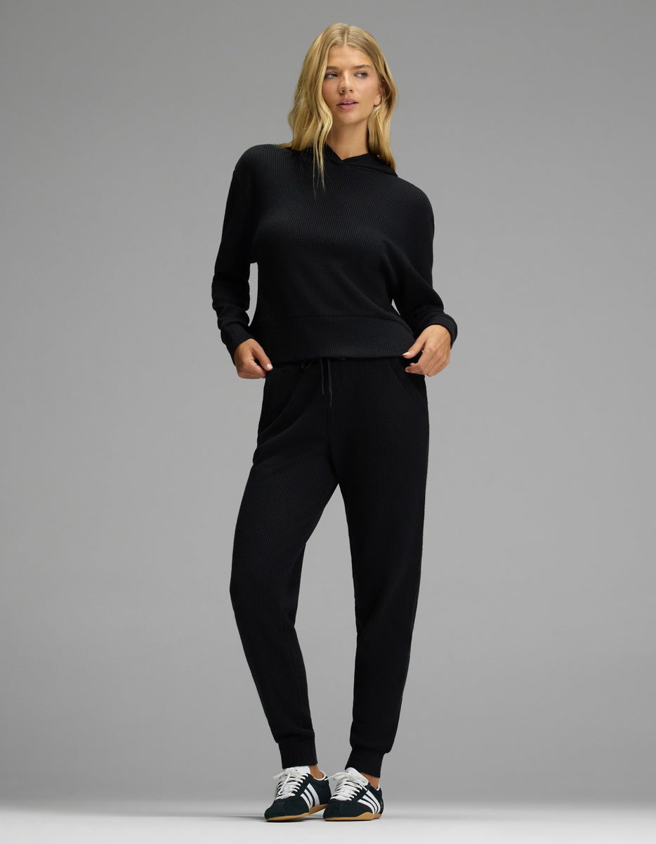 A person wearing a black Cozy Earth Women’s Blake Waffle Hoodie & Jogger Set, featuring a waffle-knit long-sleeve hooded top and matching joggers.|Color:Jet Black