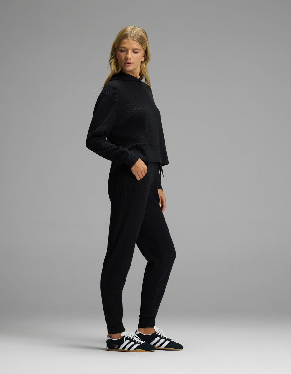 A woman wearing a black Women’s Blake Waffle Hoodie & Jogger Set with cuffed ankles and black-and-white sneakers.