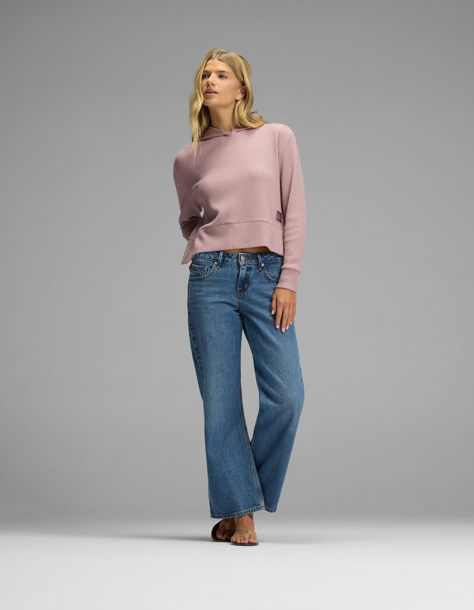 A person wears a dusty pink Women’s Blake Waffle Hoodie with long sleeves, paired with medium-wash blue jeans and sandals.