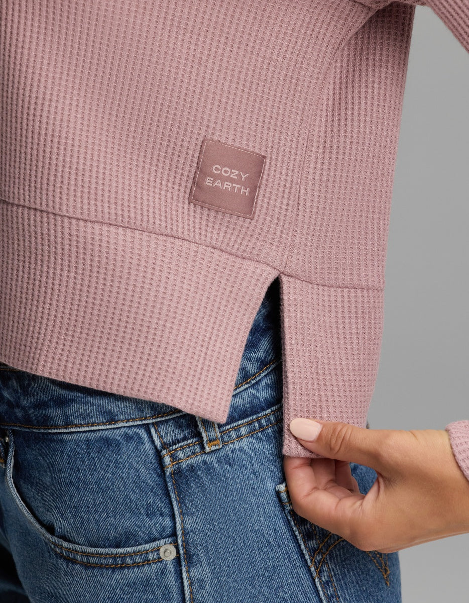 Close-up of a dusty rose Women’s Blake Waffle Hoodie with a square brand patch on the lower side, shown with a side vent tucked into blue jeans.