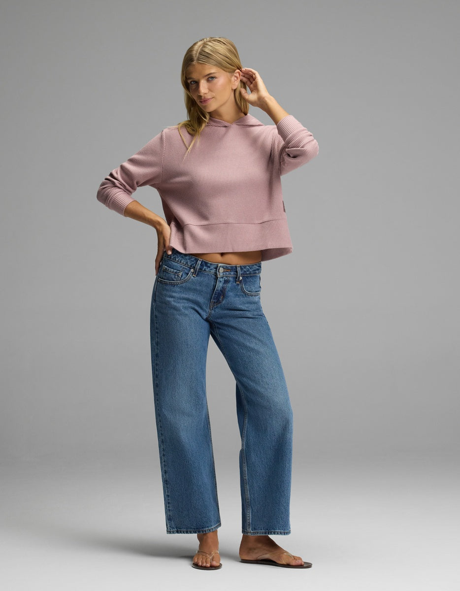 A woman wearing a mauve long-sleeved Cozy Earth Women’s Blake Waffle Hoodie and wide-leg blue jeans.