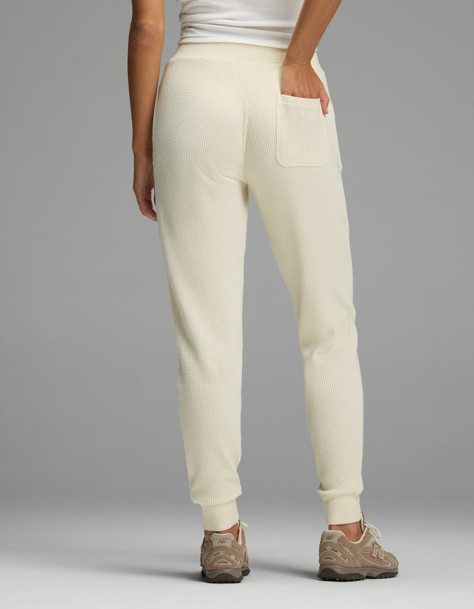 Rear view of a person wearing cream-colored Women’s Blake Waffle Jogger pants with a back pocket and beige sneakers.