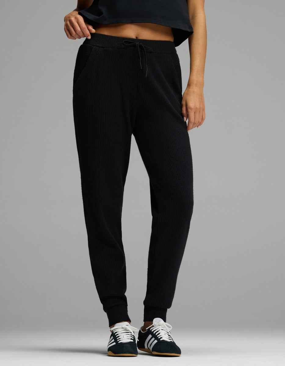 A person wearing black Women’s Blake Waffle Jogger pants with a drawstring waist and ribbed cuffs, paired with black and white sneakers.