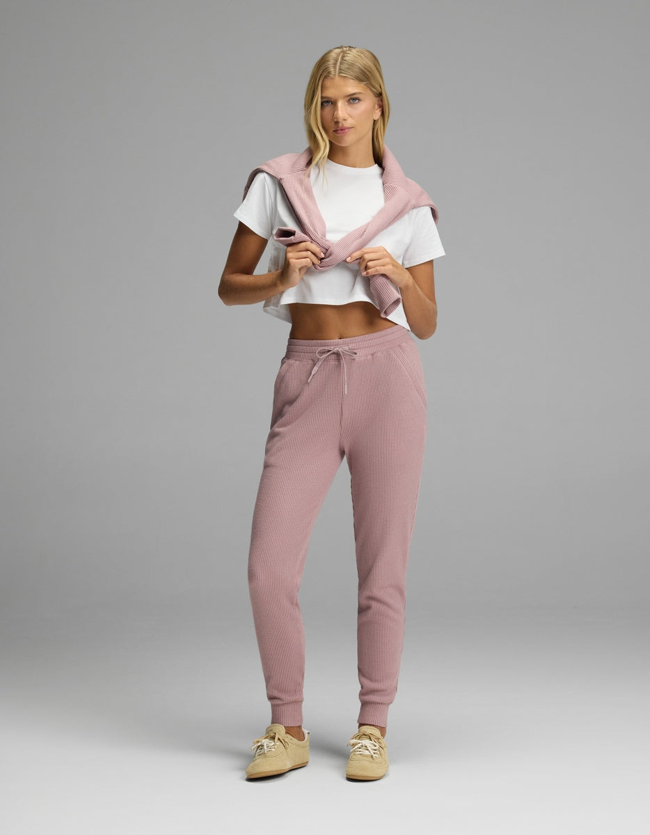 A person wearing a white t-shirt, a pink sweater draped over their shoulders, and pink textured Women’s Blake Waffle Jogger pants with a drawstring waist.