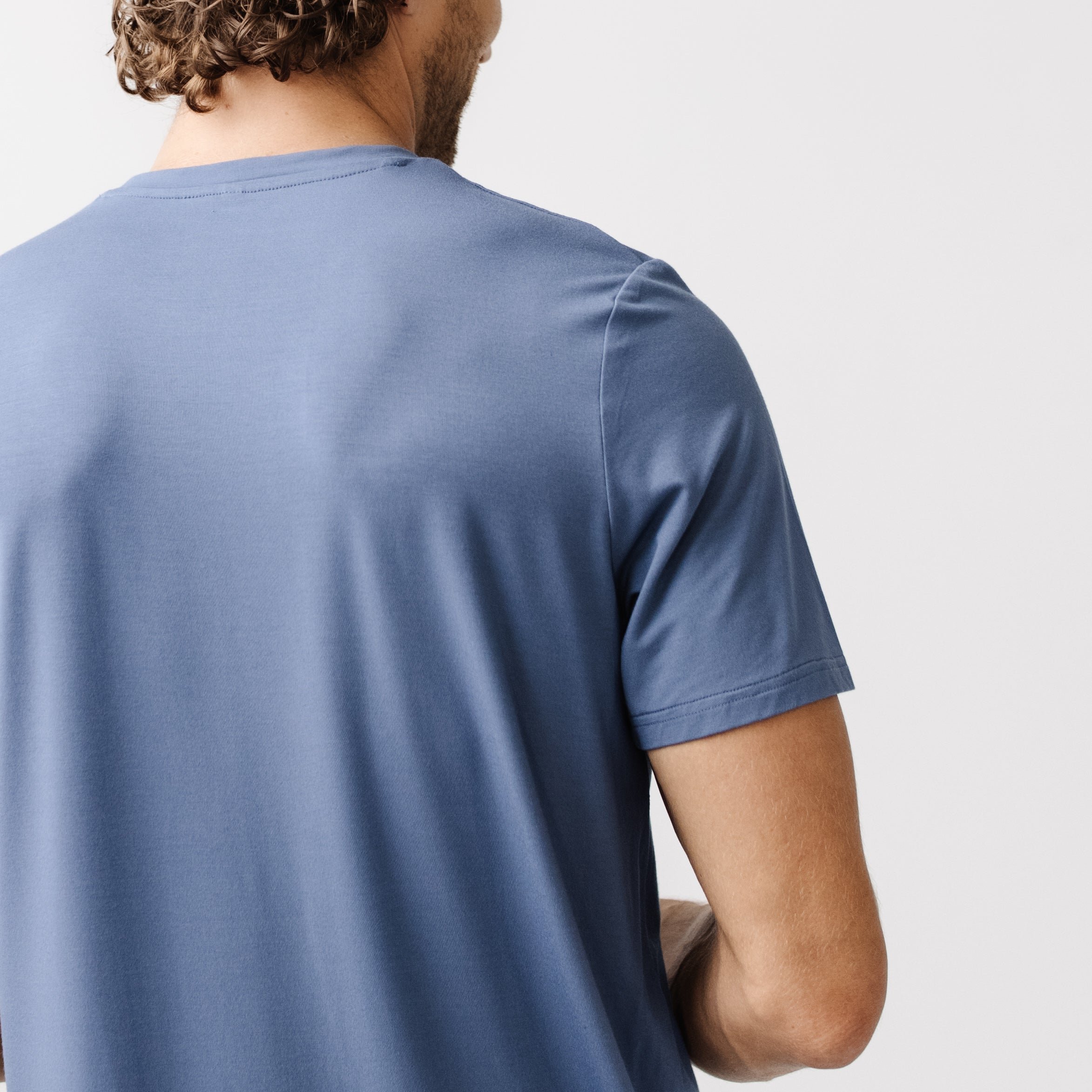 Blue Men's Stretch-Knit Bamboo Lounge Tee. A man is wearing the lounge tee in a well lit home with his back facing the camera.