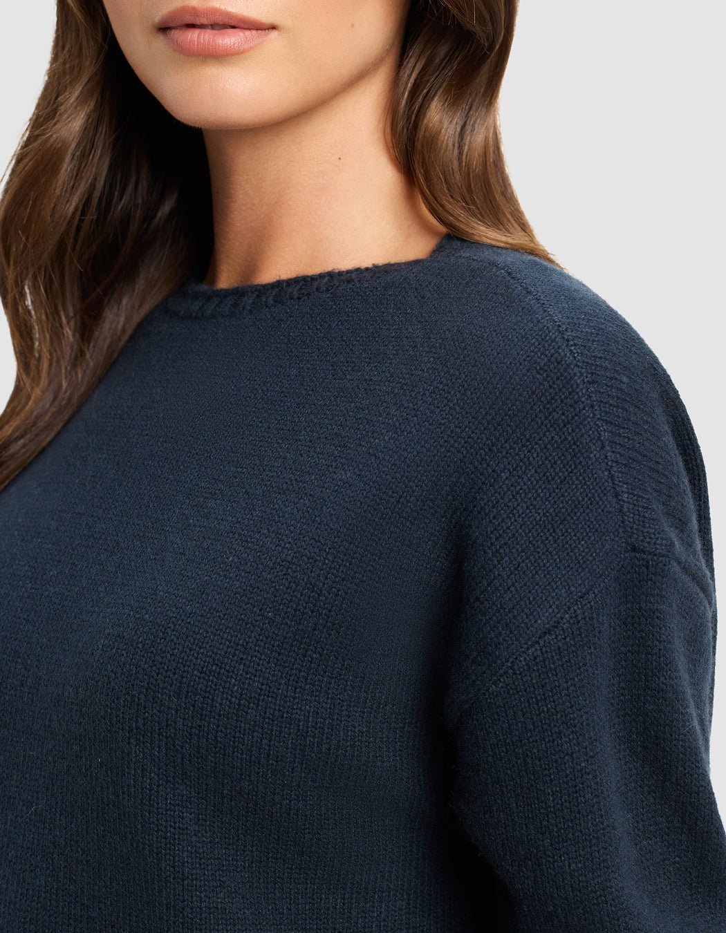 A woman with long brown hair is shown from the shoulders up, wearing the Cozy Earth Women's Brooklyn Sweater Dress in dark blue against a neutral background.