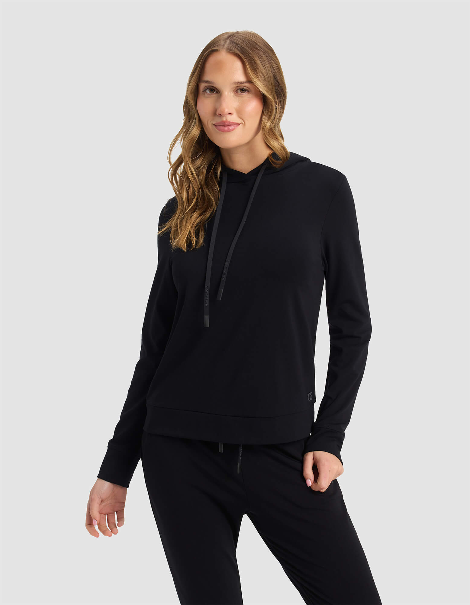 A woman with long, wavy hair wears the Cozy Earth Women's Brushed Bamboo Hoodie in black, posing against a plain light gray background.