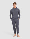 A young man stands barefoot against a plain background, hands in pockets, wearing the Cozy Earth Men's Brushed Bamboo Hoodie & Jogger Set in dark gray, and looks directly at the camera.|Color:Graphite