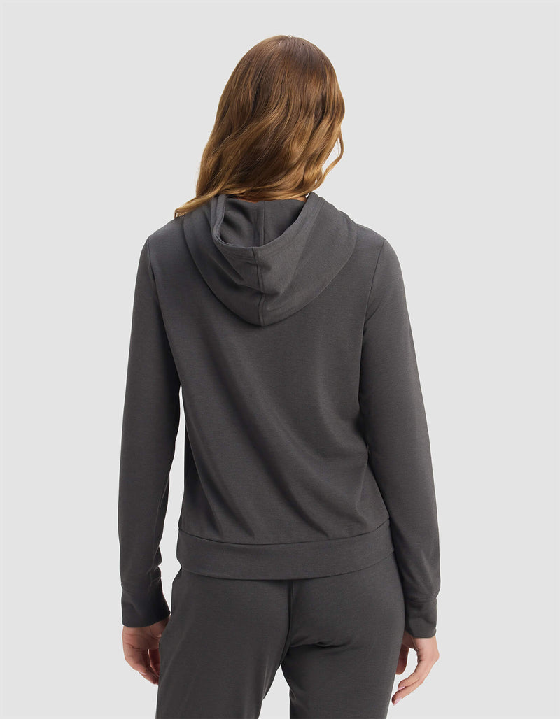A woman with wavy, light brown hair is seen from behind wearing Cozy Earth's Women's Brushed Bamboo Hoodie in dark gray against a plain, light background.