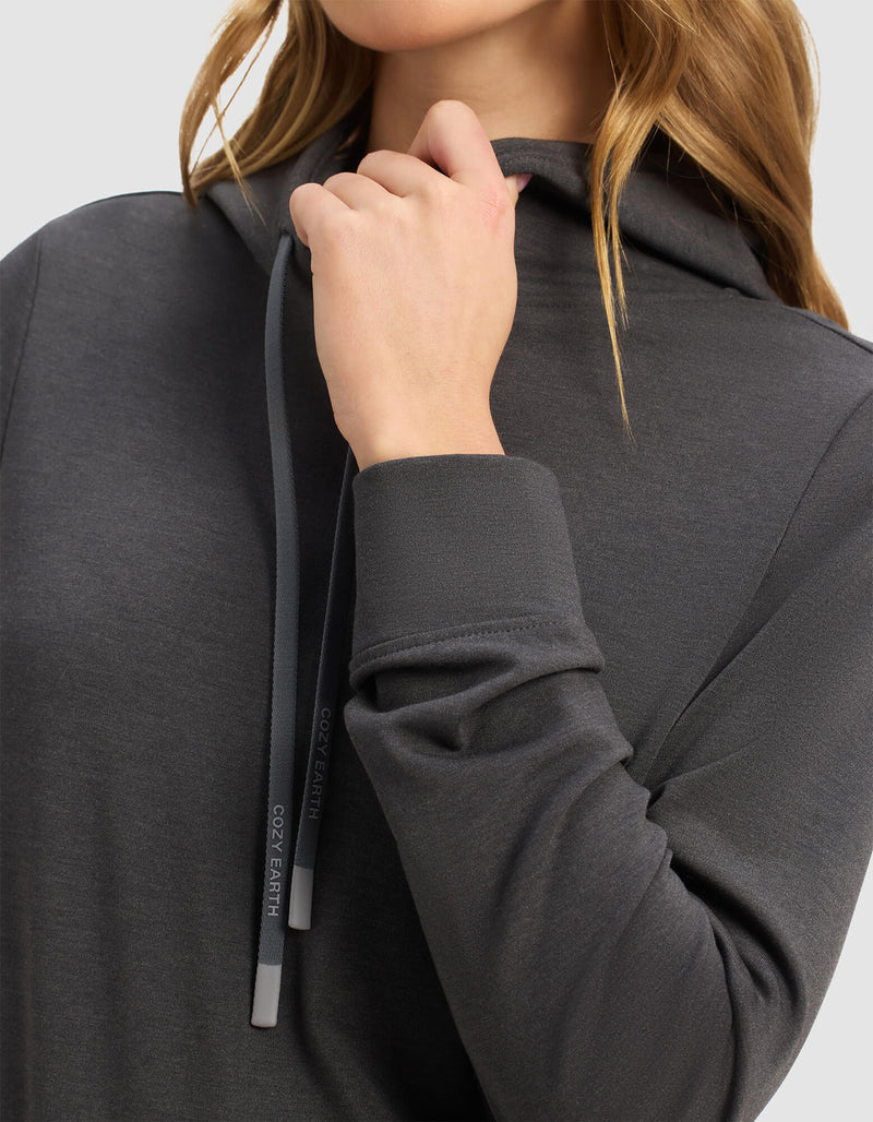 A woman models the Cozy Earth Women's Brushed Bamboo Hoodie in dark gray, holding the branded drawstrings near her chin. The soft fabric is visible, with only her lower face and upper body shown.