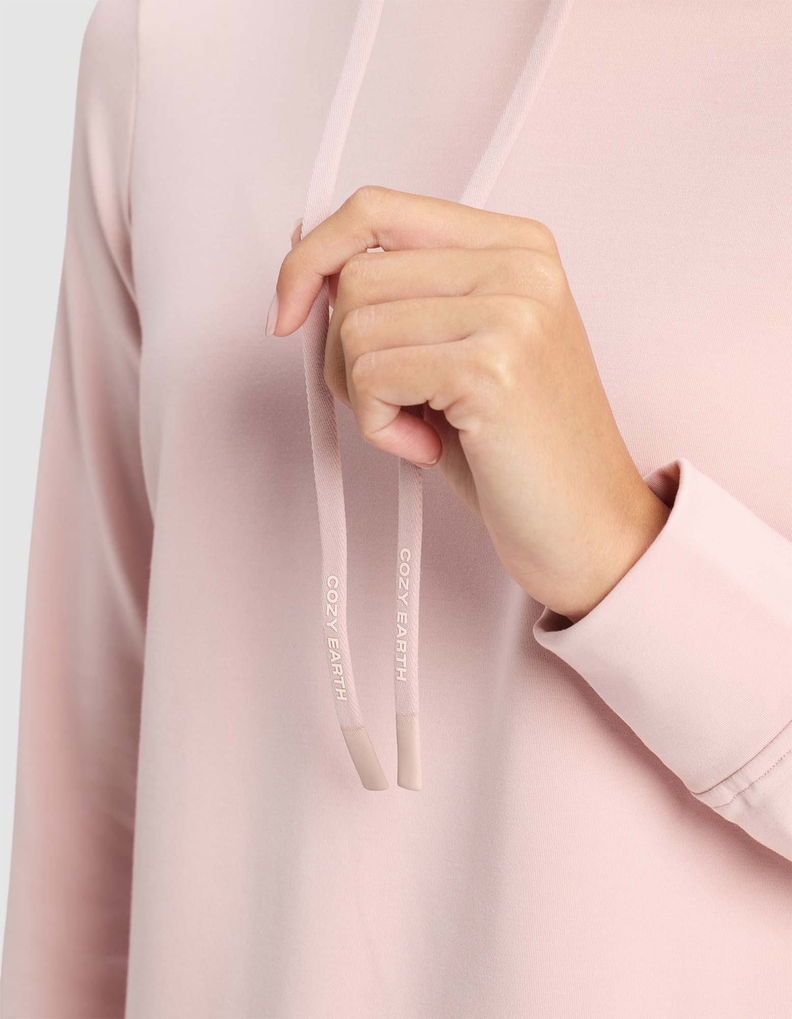 Close-up of a hand holding a pink drawcord with a visible Cozy Earth logo. 