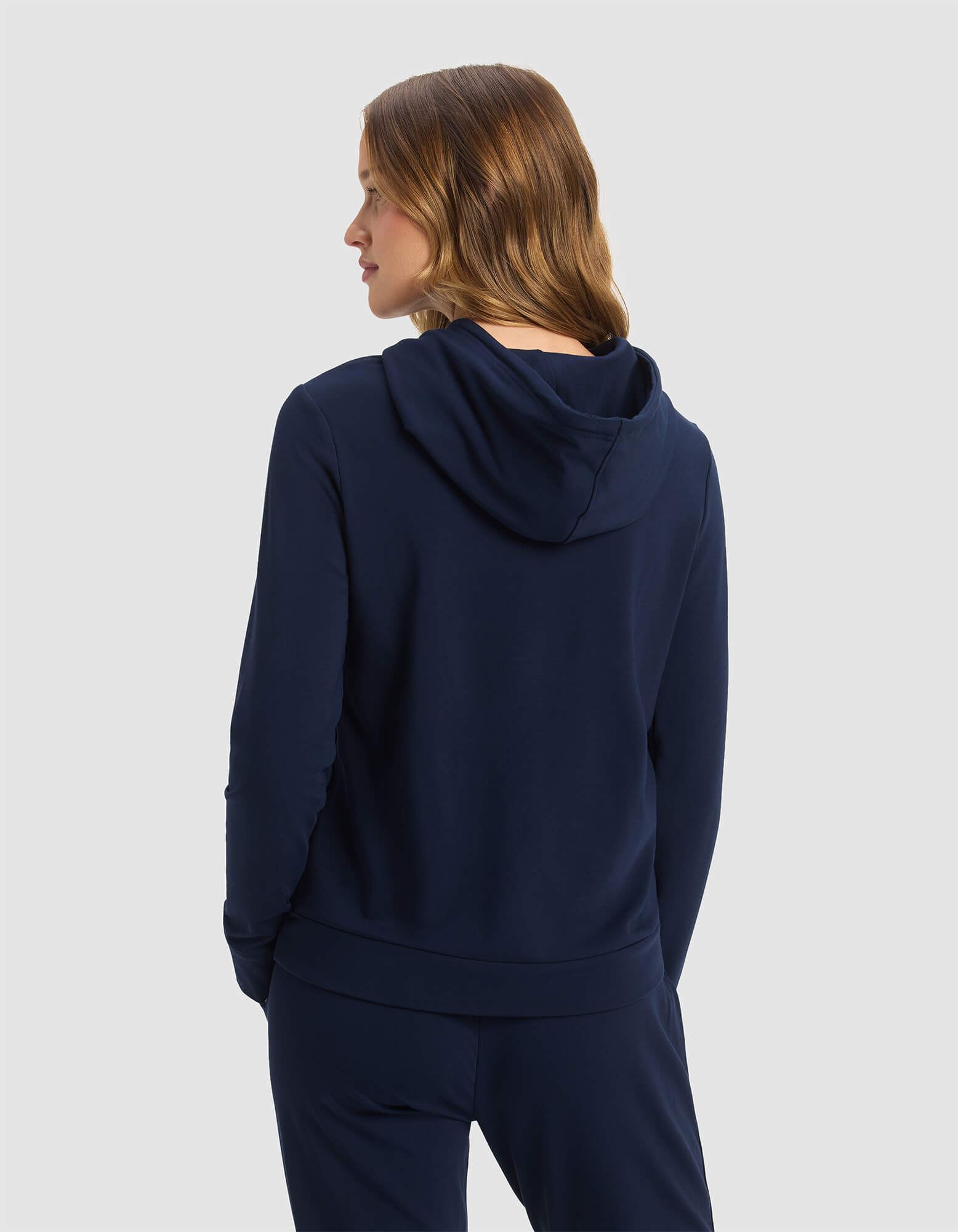 A woman with light brown hair models the Cozy Earth Women's Brushed Bamboo Hoodie in navy blue, standing sideways against a plain light gray background.|Color:Navy